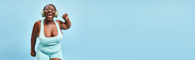 happy plus size african american woman dancing in active wear with headphones on, banner