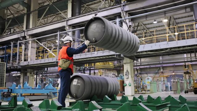 Industrial Manufacturing. A Worker is Supervising the Barrels with fuel. Fuel Barrels are Being Slowly Lowered Down. A Laborer is Controlling the Fuel Barrels by holding on to it. Production Process.