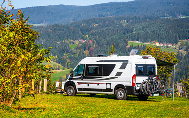 Campervan or motorhome with bicycle rack parked in the nature countryside. Camper van or  motor home is camping in a meadow surrounded by forest and hills. Active family vacation in Slovenia.