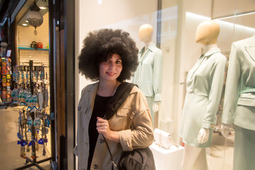 girl with curly hair near a bright store window with a bag on her shoulder