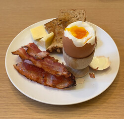 A healthy breakfast of an egg in an egg cup with bacon and toast
