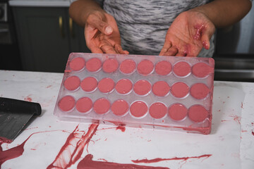 Kitchen work surface. Pink chocolate is poured into a plastic mold. Thickened chocolate spill. A woman is holding a plastic mold filled with pink chocolate.