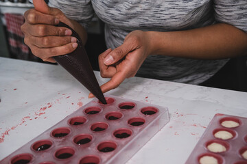 A chef or chocolatier prepares sweet chocolates at home. Close-up of the chocolatier's hands pouring chocolate into the molds. The chef's pastry bag pours hot melted chocolate into a plastic mold.
