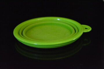 Green folding and multifunctional rubber plate, a bowl with a plastic edging on a black glossy surface.