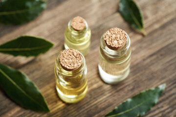 Three transparent bottles of essential oil with fresh bay leaf