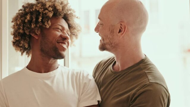 An intimate moment as a diverse gay couple shares a kiss by the window, expressing love and affection in the soft morning light.