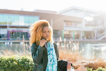 A black girl with afro hair holds shopping bags outside a shopping center, looking at camera