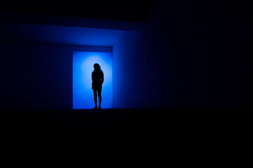 Une silhouette de femme bleu debout dans un décor architectural sombre et bleu - obrazy, fototapety, plakaty