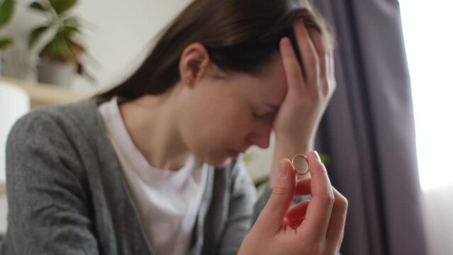 Selective focus of worried sad young woman taking off and holding wedding ring. Divorcee going through depression, apathy, heartbreak crisis. New widow feeling emotional pain, grieving after loss