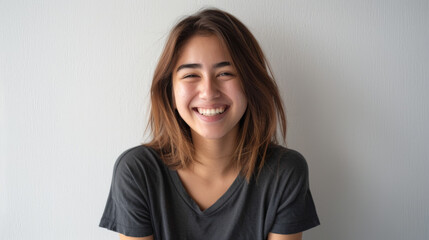 A cheerful woman with wavy hair and freckles smiles warmly, wearing a casual denim shirt against a light background. - obrazy, fototapety, plakaty