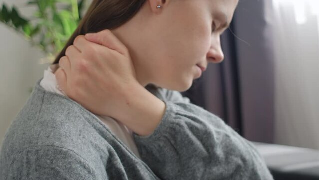 Close up of upset unhappy young caucasian woman massaging rubbing stiff sore shoulder tensed muscles fatigued, feeling hurt joint back pain ache sitting alone on sofa at home. Fibromyalgia concept