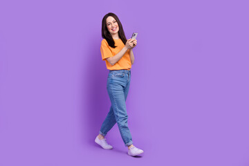 Full length body photo of strolling cheerful business woman busy browsing smartphone news feed isolated on violet color background