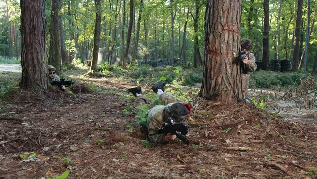 Laser tag, Precision sight, Carefully aiming. Marksman Laser tag lies prone in camouflage gear, carefully aiming paintball gun with precision sight in forested training environment.