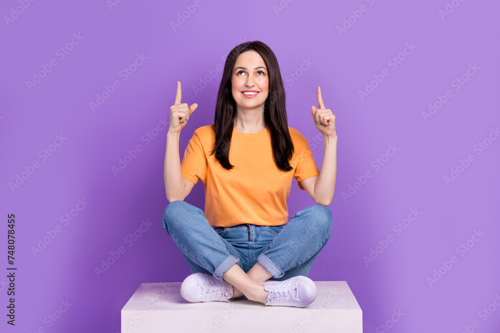 Sticker Photo of happy mature woman worker in yellow t shirt sit podium direct fingers above head proposition isolated on violet color background