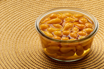 Pickled whole Biquinho Yellow chili in a glass jar on a yellow background. Sour and sweet...