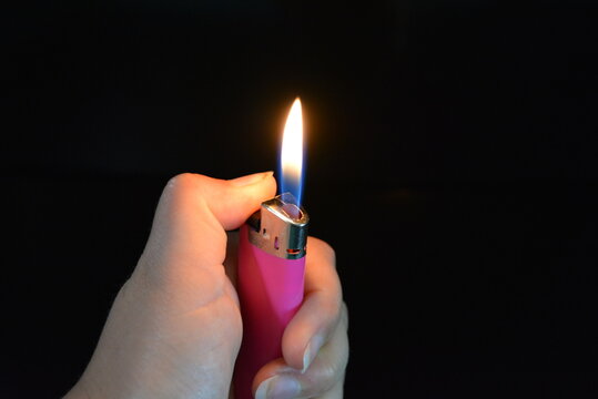 The fire and the included pink plastic lighter lie in a female hand on a black glossy surface.