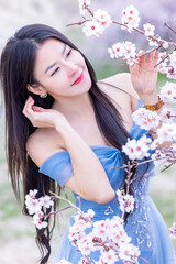Fototapeta premium Beautiful woman in blue dress on rocks mountain. Cheerful woman relax outdoor with beautiful sky and pink flowers in holiday vacation. Woman tourist enjoy amazing mountain view. Travel and freedom..
