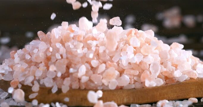 Super slow motion macro of granulated rough crystal pink himalayan salt grains are falling in wooden plate  on rustic wooden table in restaurant kitchen at 1000 fps.