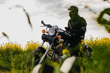 Papier Peint photo autocollant Moto male motorcyclist on a retro custom motorcycle in a blooming yellow field in summer.