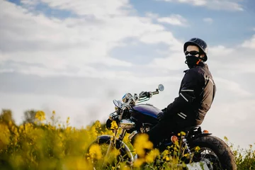 Papier Peint photo Moto male motorcyclist on a retro custom motorcycle in a blooming yellow field in summer.