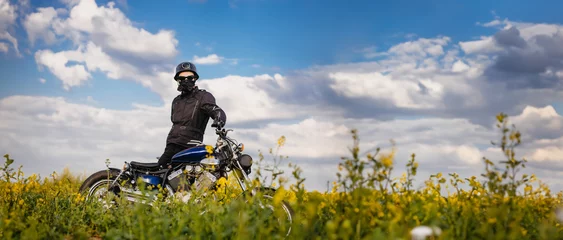 Papier Peint photo Moto male motorcyclist on a retro custom motorcycle in a blooming yellow field in summer.