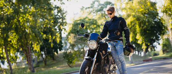 motorcyclist in outfit with motorcycle in sunglasses and jeans in summer