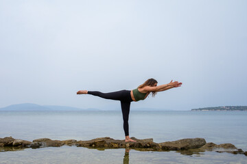 Woman practicing yoga by the sea on the rocks