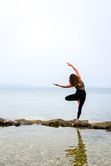 Woman practicing yoga by the sea on the rocks