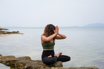 Woman practicing yoga by the sea on the rocks