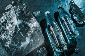 Two Bottles of water in ice on stone background. Pieces ice illuminated with blue light....
