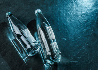 Two bottle of water on dark stone background. Advertising mineral water in glass bottle, top view - obrazy, fototapety, plakaty