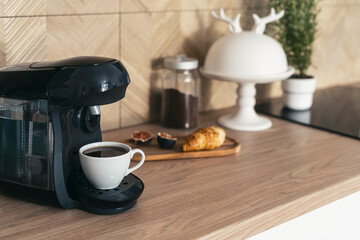 Coffee maker machine and cup with fresh drink on wooden countertop at kitchen