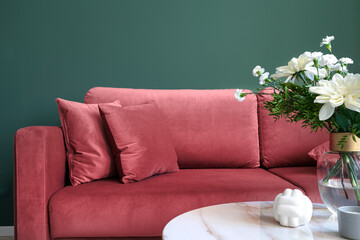 Living room interior, sofa with pillows, glass vase with flowers on side table