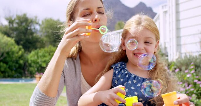 Woman, young girl in garden with bubbles and fun together outdoor, parent and child with game and toys. Liquid soap, happy mother and daughter in backyard at home, playful and smile with bonding