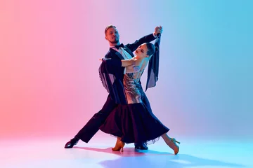 Papier Peint photo École de danse Elegant, passionate young couple, man and woman dancing ballroom in back stage costumes against gradient pink blue background in neon light. Concept of dance class, hobby, art, dance school, talent