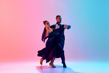 Beautiful young man and handsome woman, ballroom dancers making performance, dancing against gradient pink blue background in neon light. Concept of dance class, hobby, art, dance school, talent