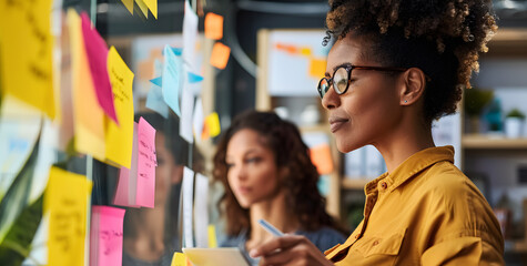 Obraz premium African American woman in her office at work exchanging ideas with her team analyzing sticky notes.