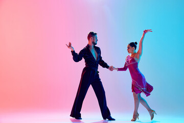 Fototapeta na wymiar Elegance and tenderness. Young man and woman, ballroom dancers in motion, dancing, performing against gradient pink blue background in neon light. Dance class, hobby, art, dance school, talent concept
