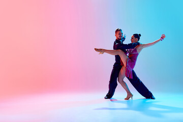 Fototapeta na wymiar Aesthetic of dance. Artistic young man and woman in motion, dancing ballroom against gradient pink blue background in neon light. Concept of dance class, hobby, art, dance school, talent