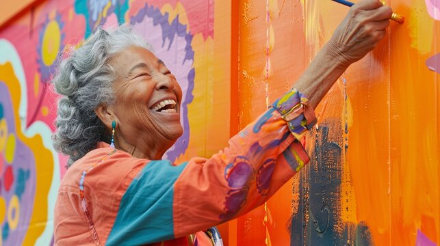 Happy elderly black woman laughs as she paints a wall orange