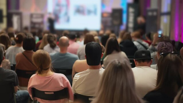Young professionals gather at an entrepreneurial event, speaker and presentation in the background blur. Youthful energy at a startup seminar. Appropriate for startup culture and business incubator