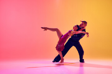 Young couple, man and woman in motion, ballroom dancers making creative performance against gradient pink yellow background in neon light. Concept of dance class, hobby, art, dance school, talent