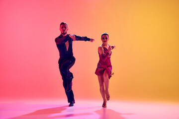 Male and female dancers performing a Latin dance in stylish clothes against gradient pink yellow...