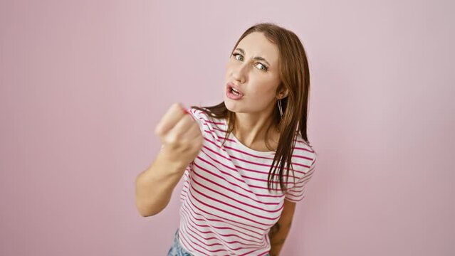 Frustrated young brunette girl in striped t-shirt, furious and mad, raising fist in anger over an isolated pink background. aggressive rage personified.