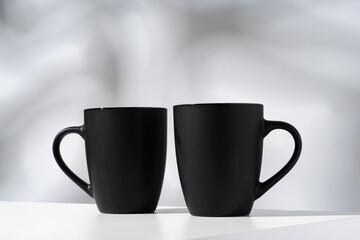 Two black ceramic mugs on gray background with shadows