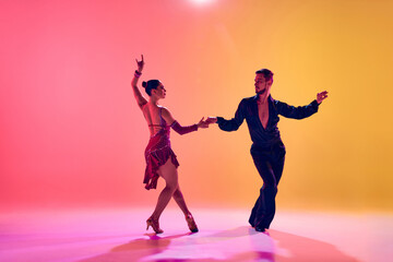Fototapeta na wymiar Male and female dancers performing a Latin dance in stylish clothes against gradient pink yellow background in neon light. Concept of dance class, hobby, art, dance school, talent