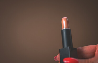 Age makeup. Red lipstick in the hand of a woman with a red manicure