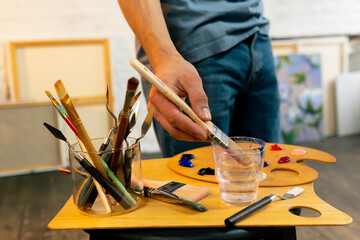close-up in an art workshop an artist in a blue T-shirt applies white paint to a palette with a palette knife