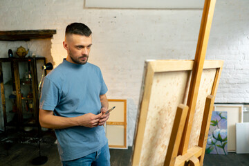 in an art workshop an artist in a blue T-shirt is thinking about where to make a stroke with...