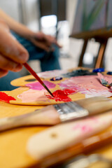 close up in an art studio an artist sitting dips a brush in red paint on a palette